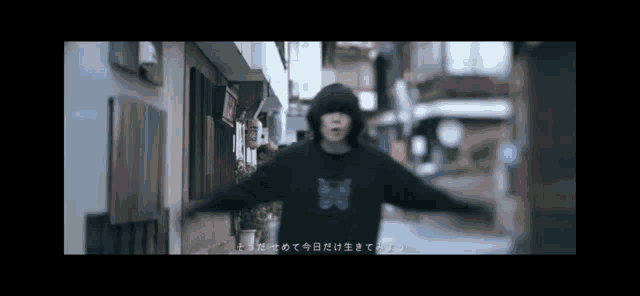 a man in a black hoodie is walking down a narrow street .