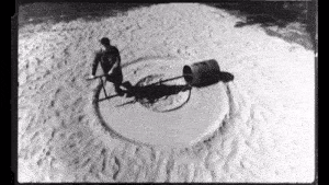a black and white photo of a man pulling a barrel in the sand .
