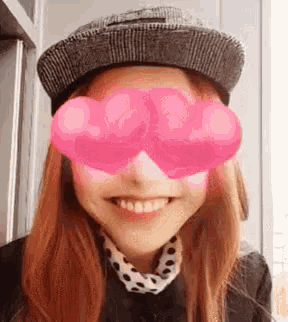 a woman wearing a hat and pink glasses with hearts on them is smiling .