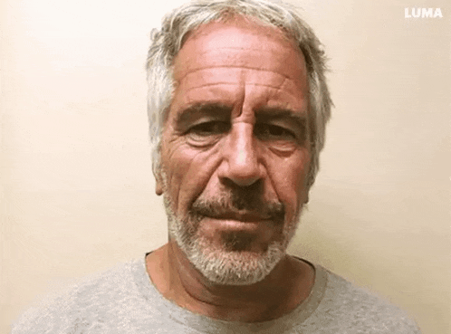a man with gray hair and a beard is standing in front of a wall and looking at the camera .