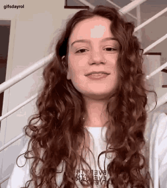 a woman with long curly hair is standing in front of a staircase and smiling .