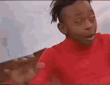 a young boy wearing a red shirt is making a funny face .