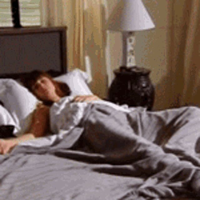 a woman is laying on a bed with a lamp and a clock on the wall