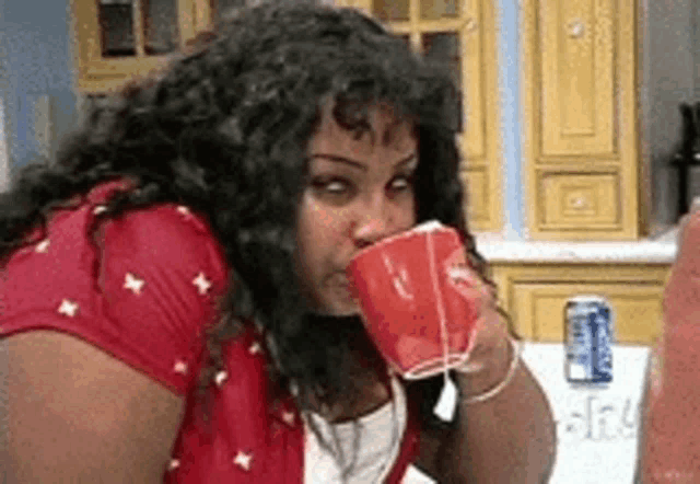a woman drinking from a red cup next to a can of diet coke