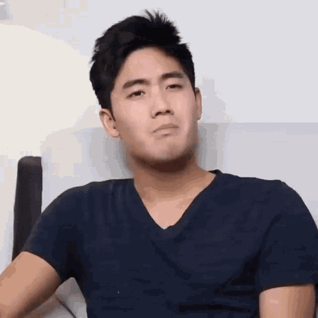 a young man in a black shirt is sitting on a couch and making a funny face