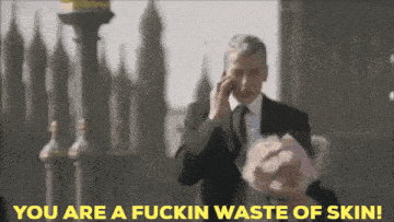 a man in a suit talking on a cell phone with the words you are a fuckin waste of skin above him