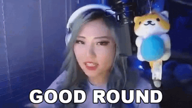a woman is sitting in front of a microphone with a stuffed animal hanging from her head and says `` good round '' .