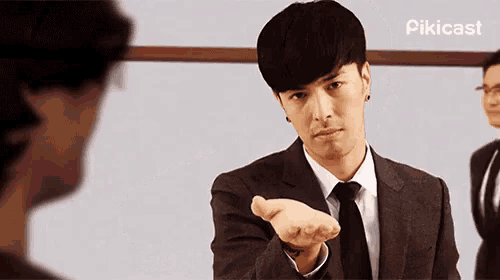a man in a suit and tie is reaching out his hand to another man .