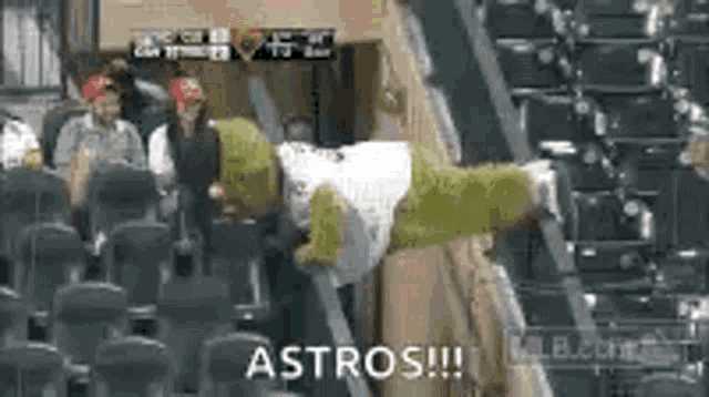 a shrek mascot is sitting in the stands at a baseball game with a group of people .