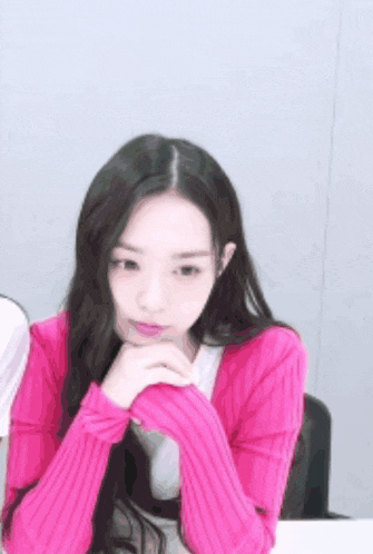 a woman in a pink sweater with her hands on her chin