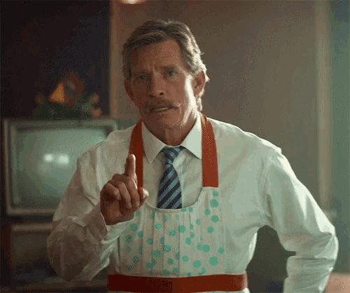 a man wearing an apron and a tie is pointing