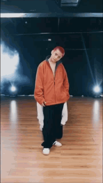 a man with red hair wearing an orange jacket and black pants