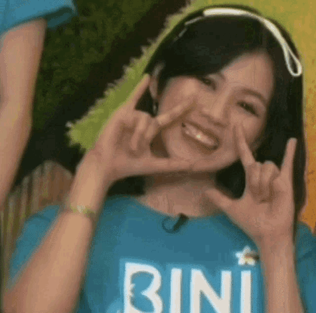 a woman in a blue shirt with the word bini on it is making a devil horns sign .