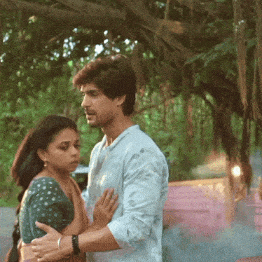 a man and a woman are hugging each other in front of trees
