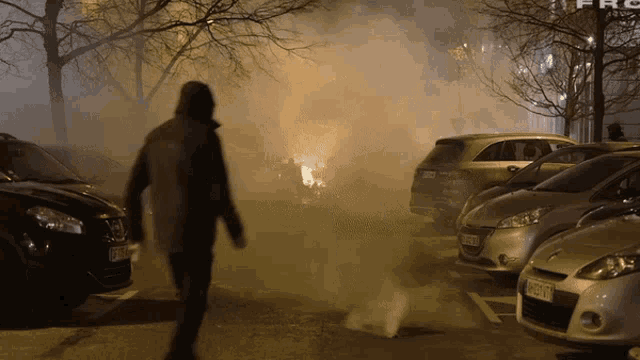 a man stands in front of a parking lot with cars parked and smoke coming from the ground