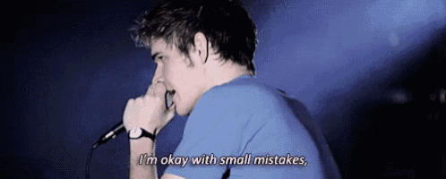 a man in a blue shirt is singing into a microphone and says i 'm okay with small mistakes .