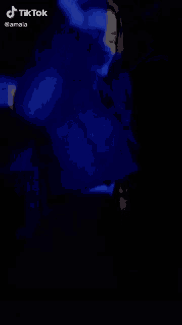 a woman in a blue sweater is dancing in the dark .