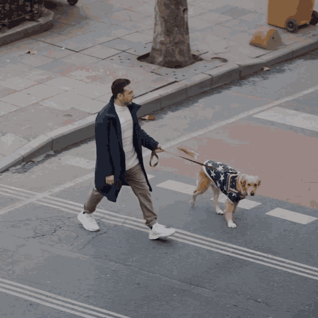 a man walking a dog that is wearing an american flag shirt