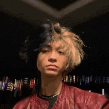 a young man with a red jacket on is looking at the camera with a blurry background