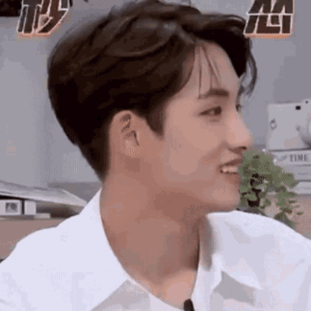 a young man in a white shirt is smiling while sitting in a room .