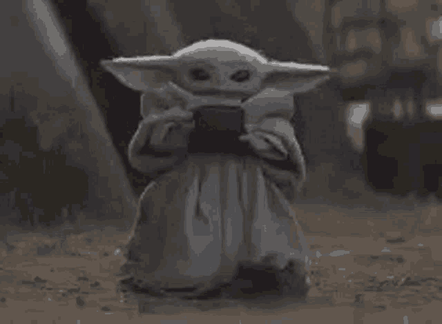 a baby yoda from star wars is holding a cell phone in his hands .