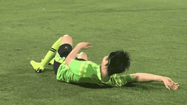a soccer player is laying on the grass with a green shirt that says x on it