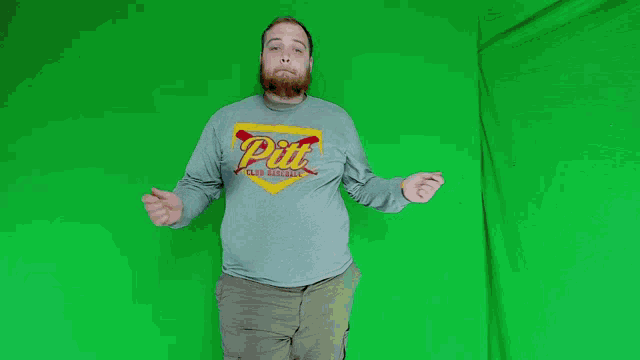 a man wearing a pit t-shirt stands in front of a green background