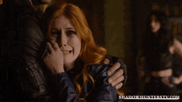 a woman is crying while being hugged by a man with shadowhunterstv.com written on the bottom