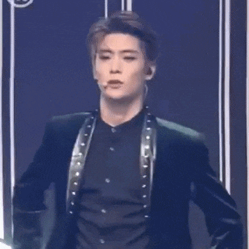 a young man in a green suit and black shirt is standing on a stage with his hands folded .