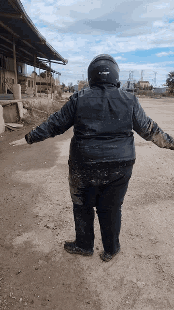 a person wearing a black ls2 helmet stands in the dirt with their arms outstretched