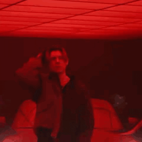 a man is standing in a dark room with a red light shining on his face .