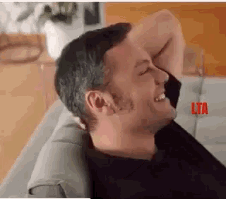 a man is sitting on a couch with his hands behind his head and laughing .