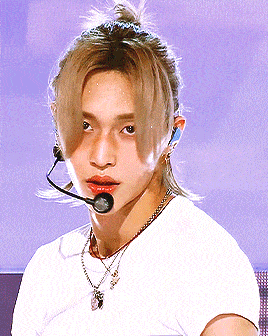a young man wearing a white t-shirt and a necklace has a microphone in his ear