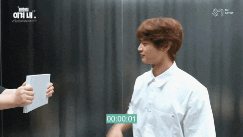 a man in a white shirt is talking to another man in front of a sign that says 00 : 00 : 01