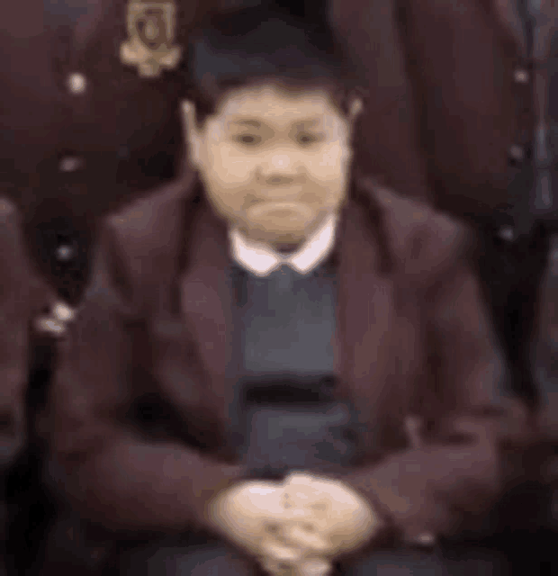 a young boy in a maroon school uniform is sitting in a group photo .
