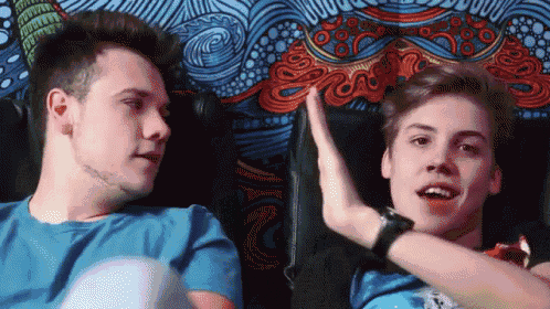 two young men are giving each other a high five while sitting in front of a colorful tapestry