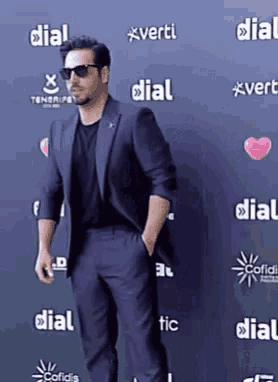 a man in a suit and sunglasses stands in front of a wall that has the word dial on it