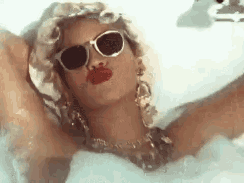 a woman is taking a bath in a bathtub wearing sunglasses and red lipstick .