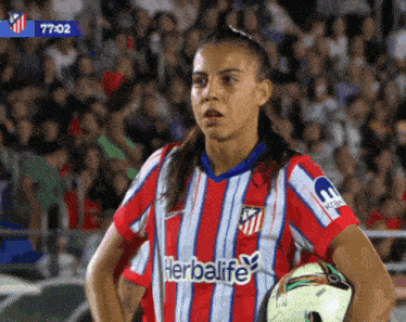 a female soccer player wearing a red and white jersey with herbalife written on it