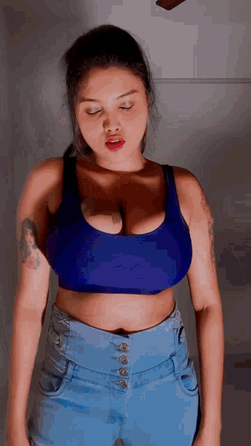 a woman in a blue crop top and jeans is standing with her eyes closed .