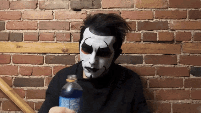 a man with a clown face painted on his face holds a bottle of soda