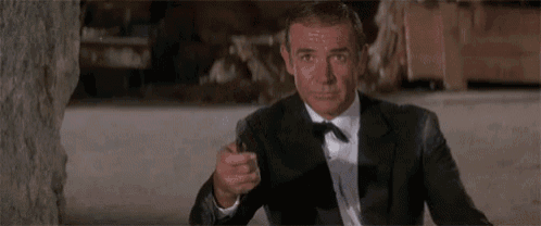 a man in a suit and bow tie is pointing a gun at someone .