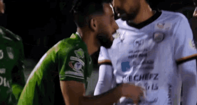 a man in a green shirt is kissing another man in a white shirt on the neck .