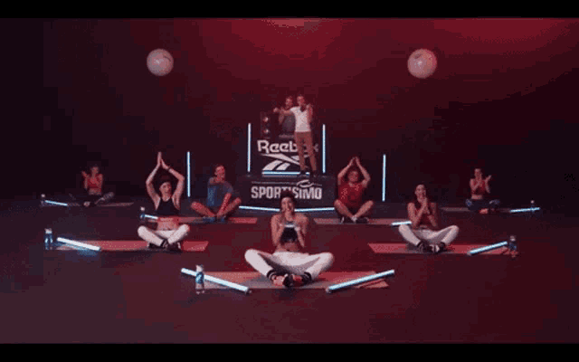 a group of people sit on yoga mats in front of a sign that says sportismo