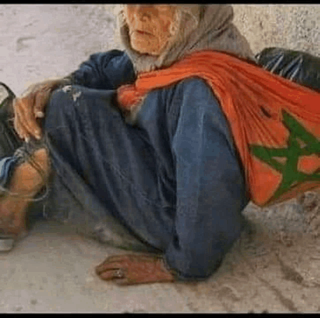 an elderly woman is sitting on the ground holding a bag .