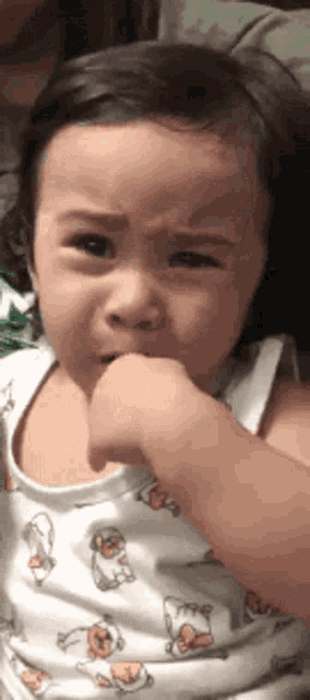 a little girl is biting her thumb while wearing a white tank top with chickens on it .