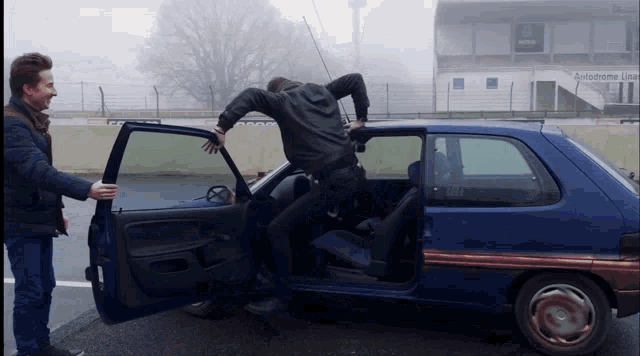 two men are standing next to a blue car that has the door open