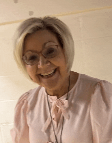 a woman wearing glasses and a pink blouse smiles for the camera