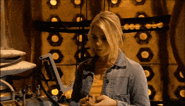 a blonde woman in a denim jacket is standing in front of a wall with circles on it