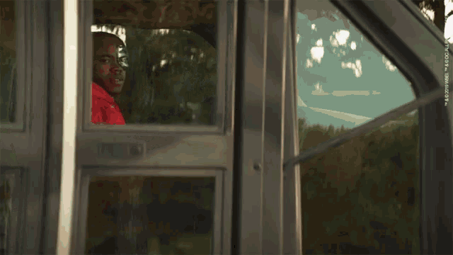 a man in a red shirt is looking out a window with a watermark that says ' adobe '